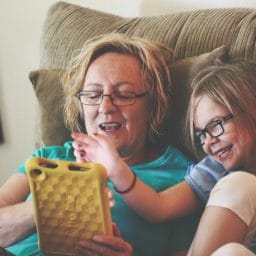 Older adult female and young girl play with a tablet while sitting in a recliner