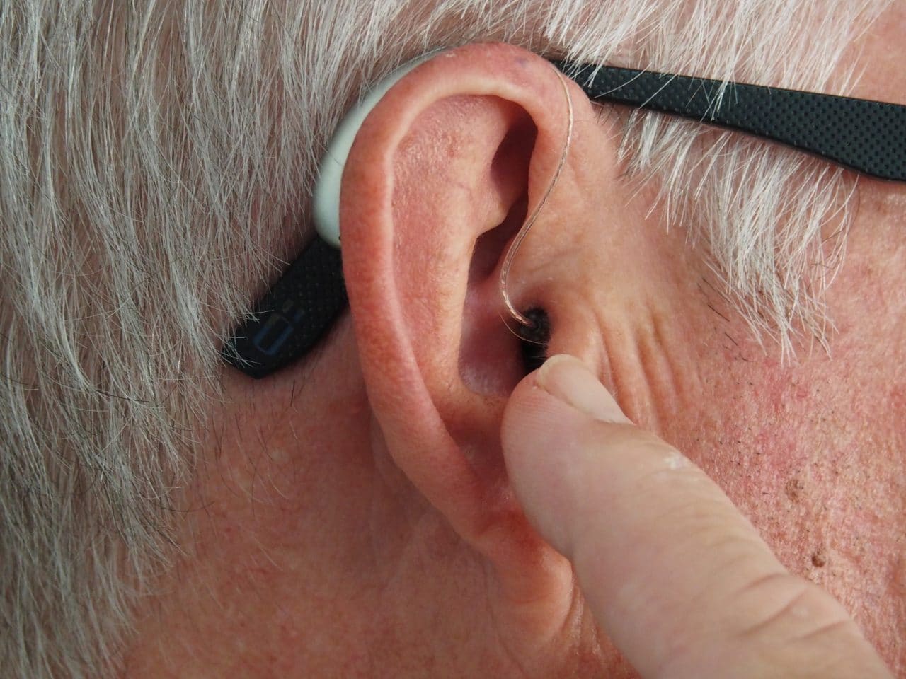 What You Should Do Before Buying Hearing Aids Man points at hearing aid on ear