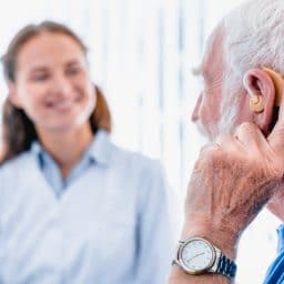 Focused picture of an elderly male patient with hearing aid side view with blurred woman doctor in the background