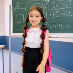 Young girl standing in front of a chalkboard on the first day of school.