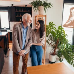 Young woman assisting elderly man with walking stick at home