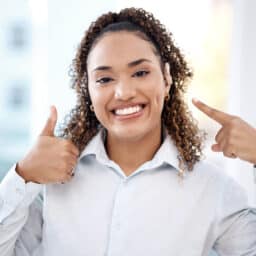 Smiling woman pointing to her hearing aid and giving a thumbs-up