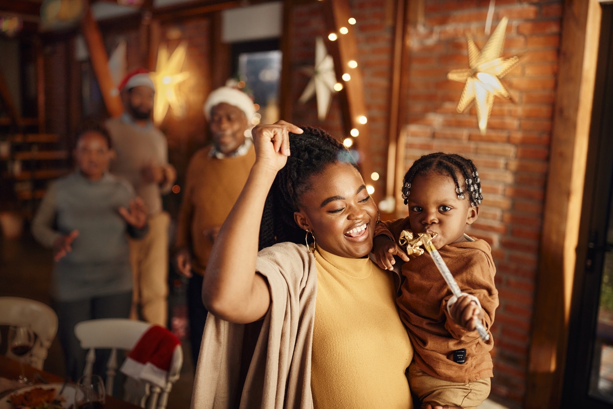 A family celebrates the holidays at a holiday party. A dancing woman holds a child.