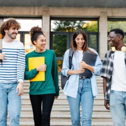 Smiling group of students walking across college campus.