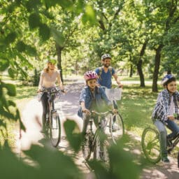 Happy family of four riding their bikes through the park on a sunny day.