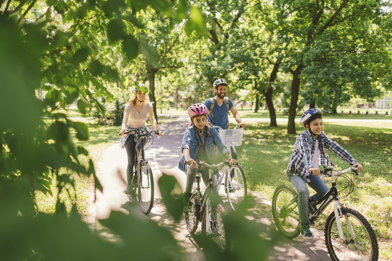 Happy family of four riding their bikes through the park on a sunny day.
