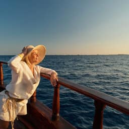 Stylish woman on a cruise standing on the boat deck looking at the waves.