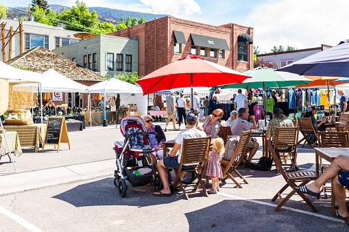 Crowd of people enjoying a local street fair and outdoor market in a quaint neighborhood on a summer day.