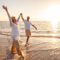 Happy senior man and woman old retired couple walking and holding hands on a beach at sunset