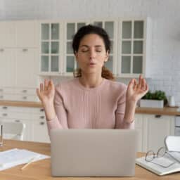 Businesswoman sit at table in kitchen near computer closed eyes makes breathing technique calming exercises.