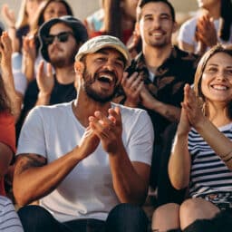 Group of people watching a sport event and cheering. Excited crowd of sports fans applauding sitting in stadium.